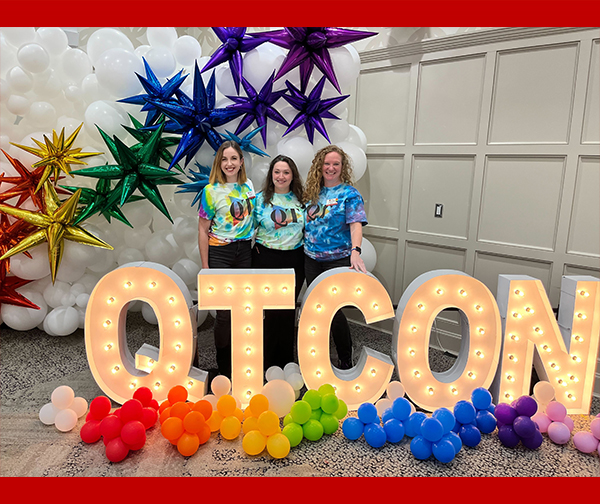 Three organizers of QT-CON stand beside the lit QT-CON sign.