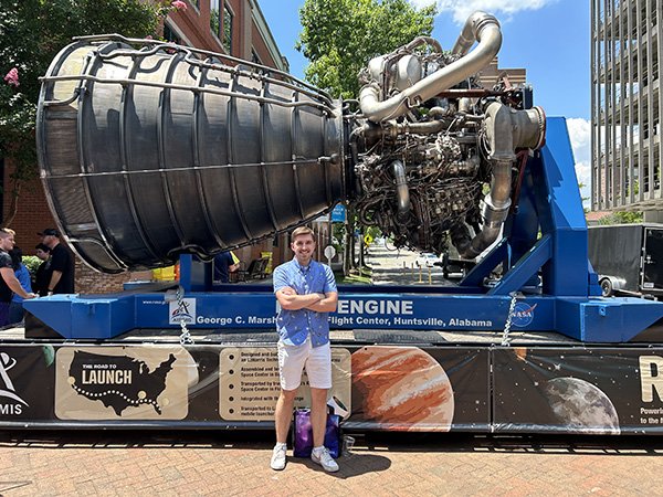 Bradley Gartner stands in front of a rocket engine during his NASA internship.