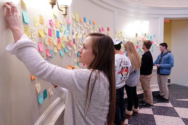 Students in the Farmer School of Business put post-it notes on a board.