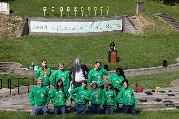 a group of volunteers in green shirts pose in Ernst Nature Theatre with the grass stage behnind them and the words read literature at Miami spelled out on a banner