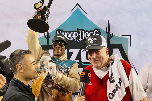 Miami University football coach Chuck Martin talks after the Arizona Bowl victory by the RedHawks while Snoop Dogg holds up the bowl trophy.