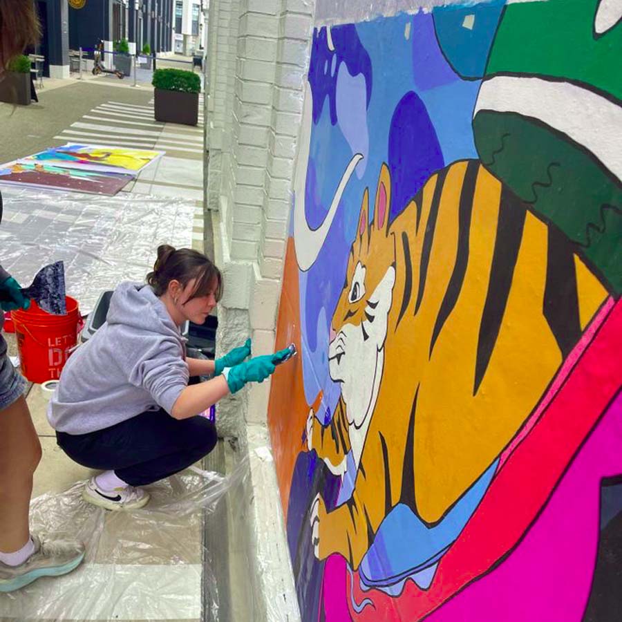 Students work on installing a mural panel at Newport on the Levee