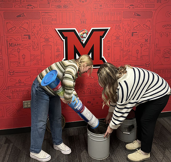 Annabel and Alex pour batteries form collection bin into metal bucket at the UCM office