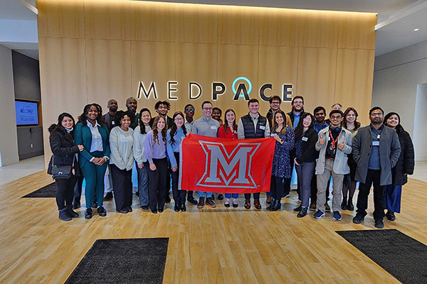 PCLS participants pose for a picture with a Miami University flag in front of a Medpace logo.