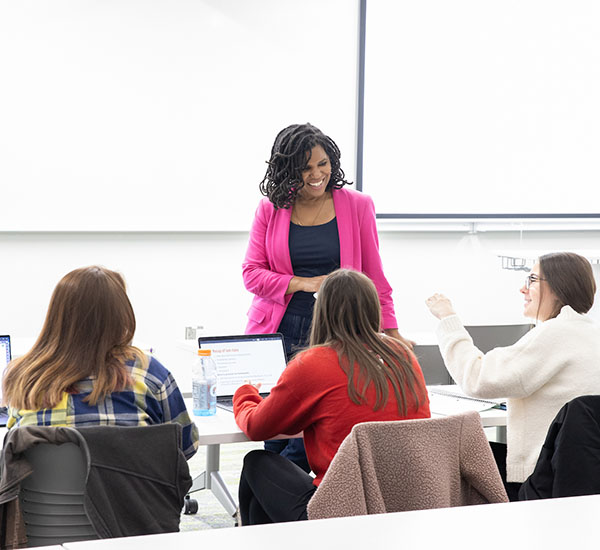 Amber Franklin in a classroom smiles and talks with 3 students sitting at tables 