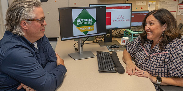 Jeff Shaver, left, senior organizational development consultant, and Natalie Skoumbros, right, director of benefits services, talk in front of a computer screen displaying Miami University's status as a 2026 Healthiest Employer in Ohio.