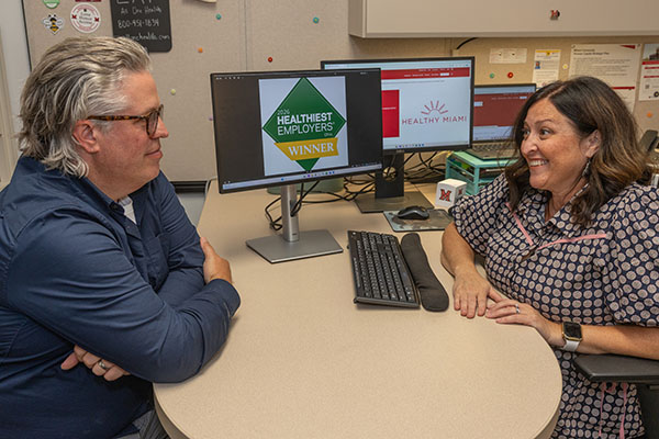 Jeff Shaver, left, senior organizational development consultant, and Natalie Skoumbros, right, director of benefits services, talk in front of a computer screen displaying Miami University's status as a 2026 Healthiest Employer in Ohio.
